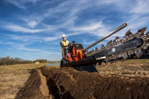 Operator using a Ditch Witch walk-behind trencher to dig a narrow trench for underground utility installation.