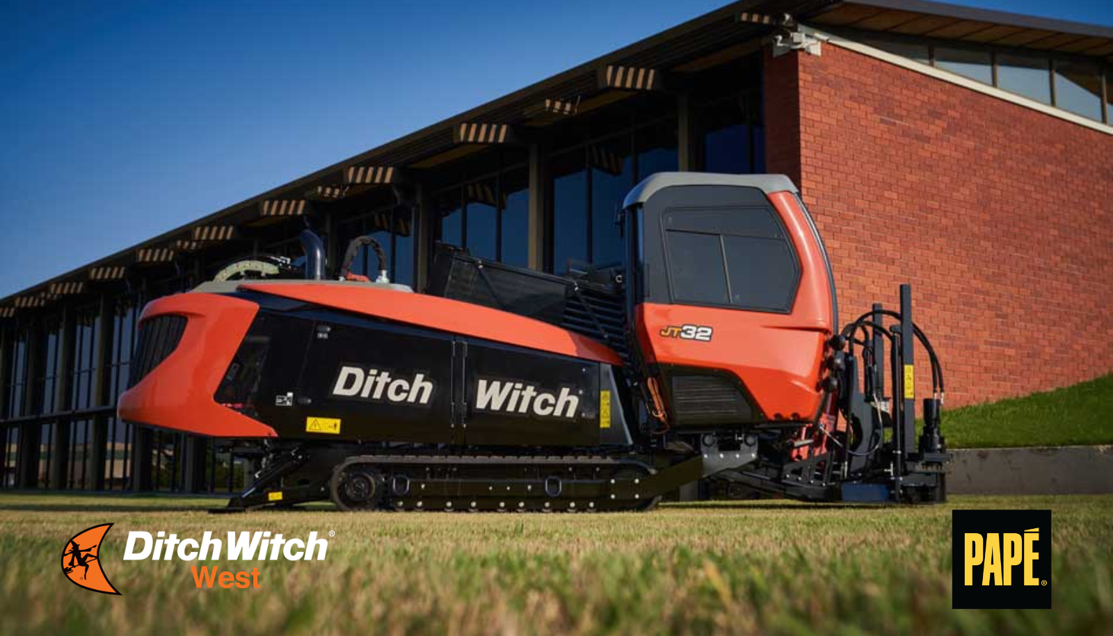 Ditch Witch JT32 horizontal directional drill positioned on grass beside a commercial building.