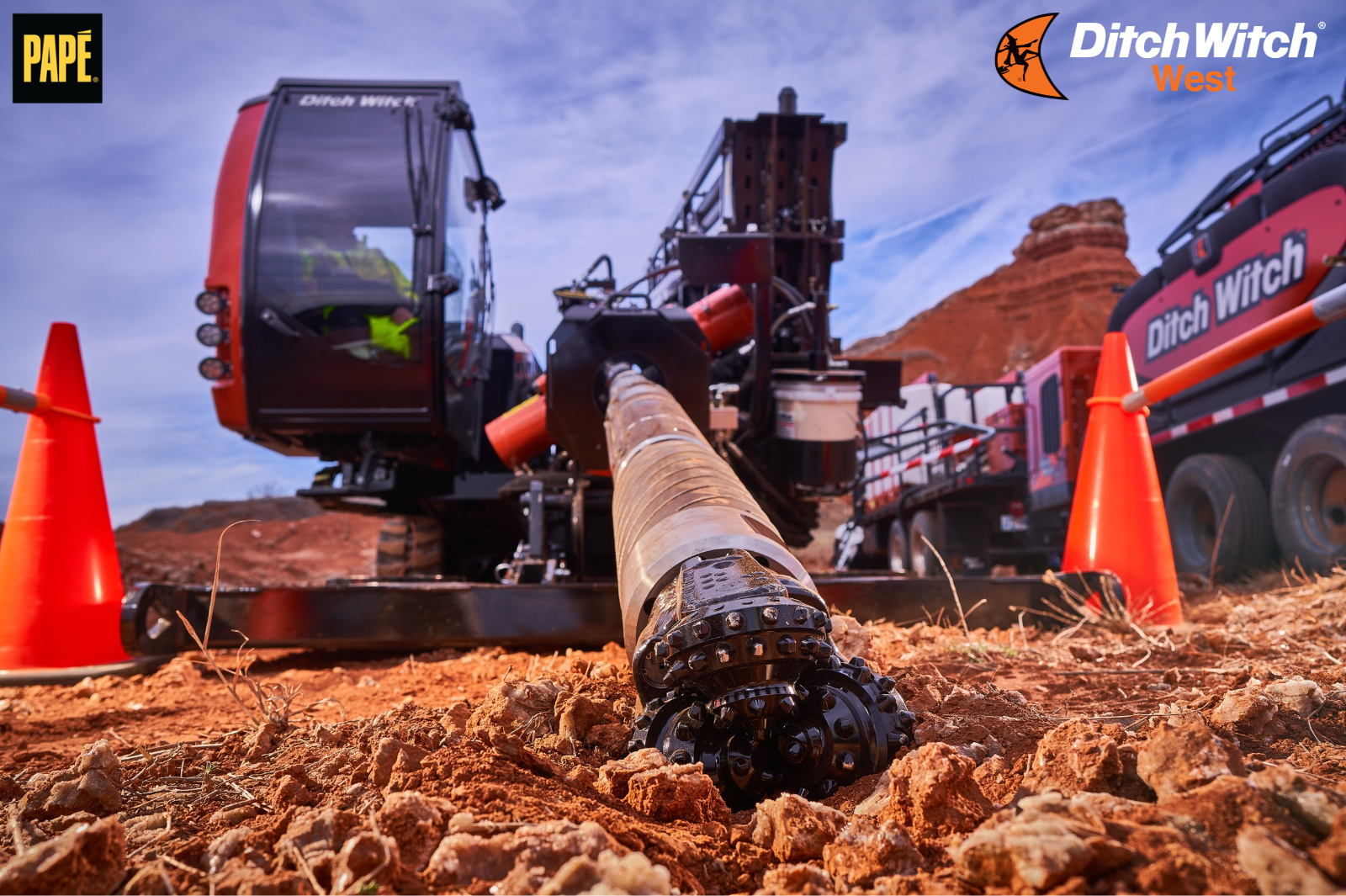Close-up of a horizontal directional drilling drill string and cutting head extending from Ditch Witch equipment at a rocky excavation site.