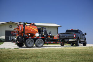 Ditch Witch vacuum excavator trailer attached to a Ford Super Duty pickup truck, parked outside a commercial building.